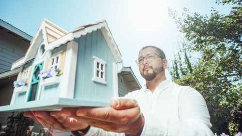 Free A man holds a miniature house model outdoors on a sunny day, symbolizing home buying. Stock Photo