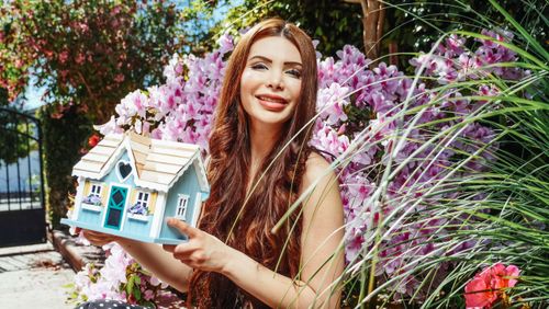 Free A woman holding a tiny house model among vibrant flowers in a sunny garden scene. Stock Photo