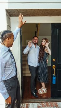 A couple waves hello to their realtor, embodying joy in new home ownership. Real estate success!