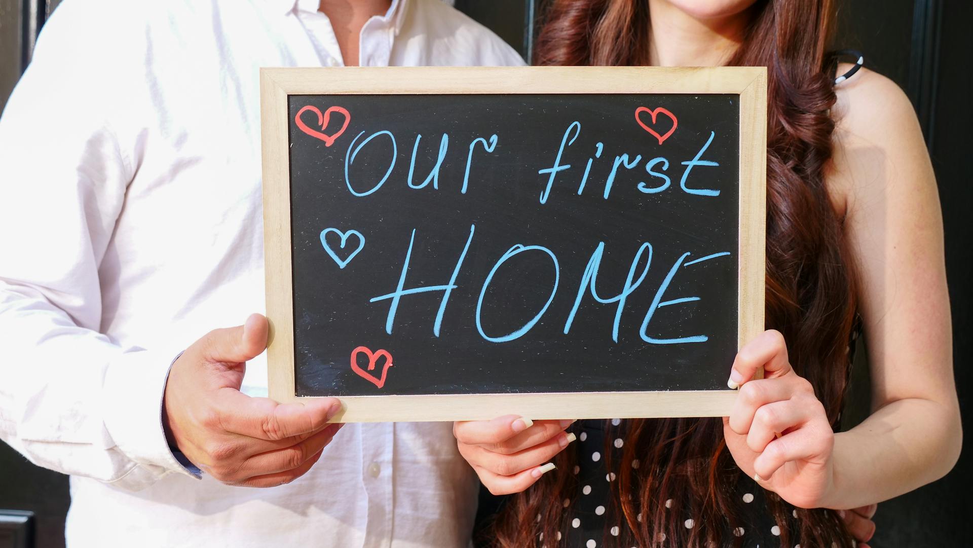 Happy couple holding a chalkboard sign celebrating buying their first home together.