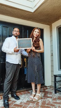 Smiling couple holding 'Welcome Home' sign at their new residence.