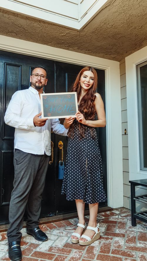 Free Smiling couple holding 'Welcome Home' sign at their new residence. Stock Photo