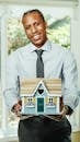 Man in Dress Shirt Holding Miniature Wooden House