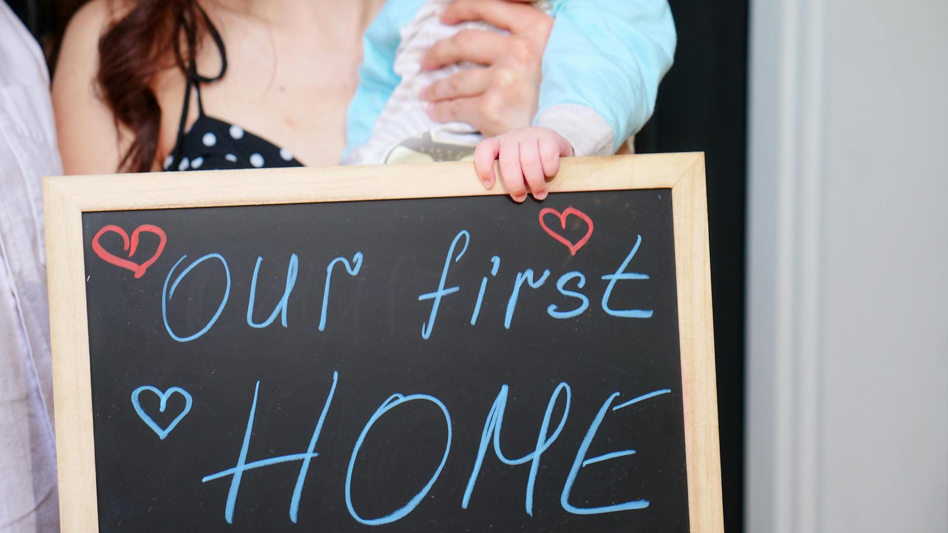 A joyful family announces their first home with a heartfelt chalkboard sign.