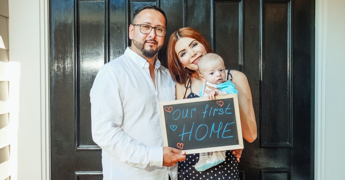 Young family holding sign celebrating their first home purchase. Joyful and heartwarming moment.