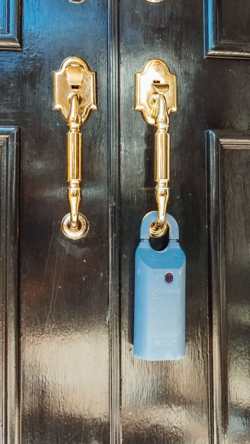 Blue key lockbox hanging from the handle of a black front door