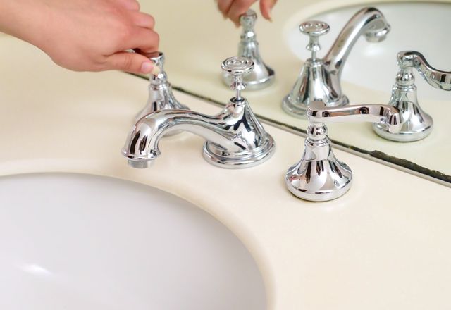 Hand adjusting a chrome bathroom faucet
