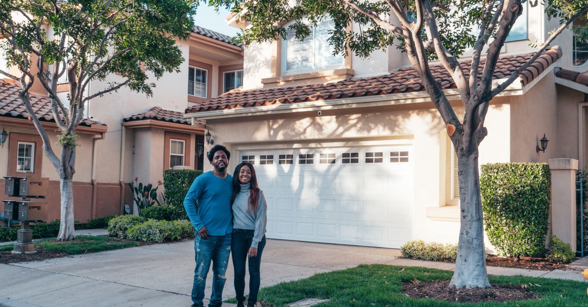 A smiling couple proudly posing in front of their newly purchased house, expressing joy and togetherness.