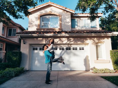 A joyful couple celebrating in front of their newly purchased house on a sunny day.