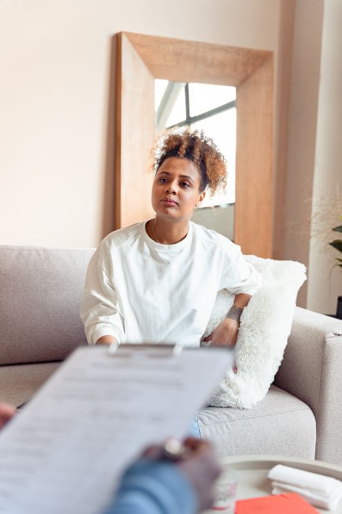 Free A woman engages in a thoughtful discussion during a therapy session, seated on a couch. Stock Photo