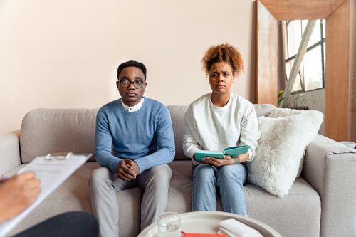 Free A couple sits on a sofa during a therapy session, appearing concerned. Stock Photo