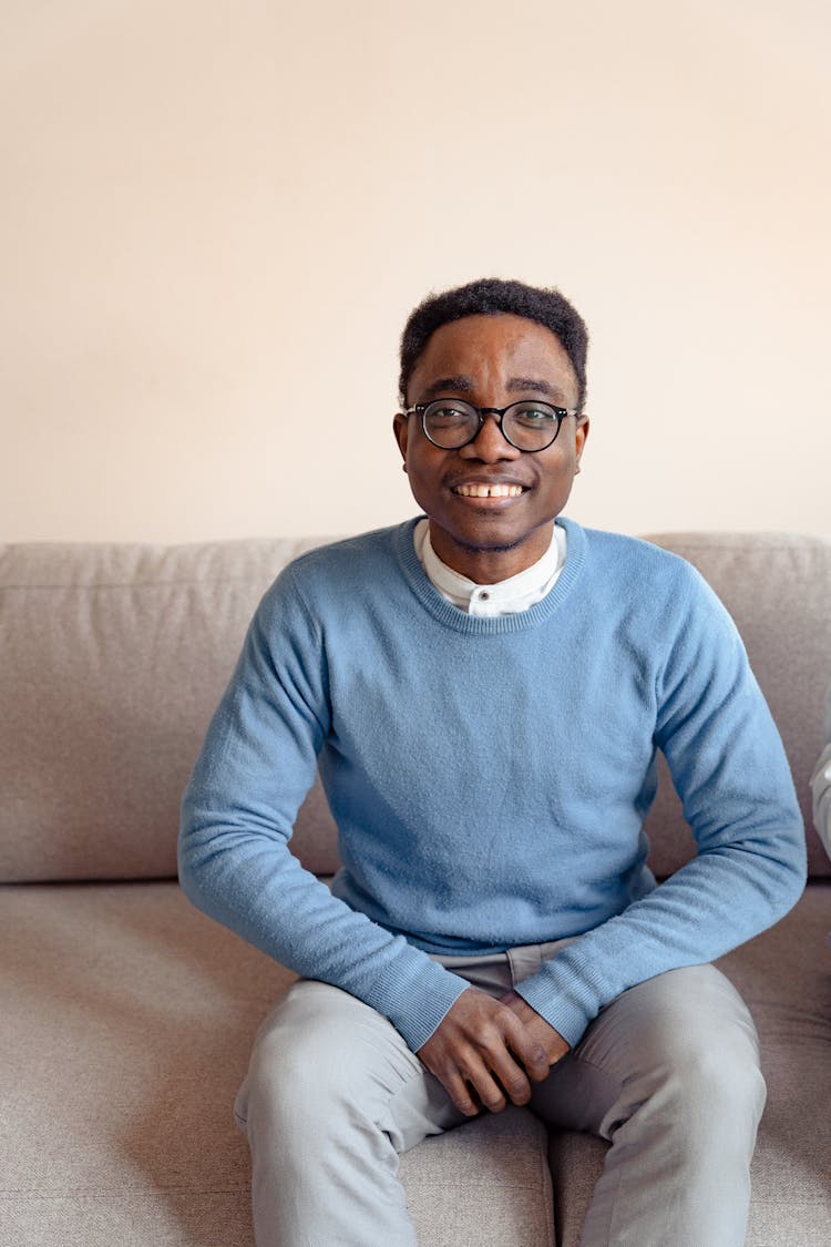 Man In Blue Sweater Smiling While Sitting On A Couch