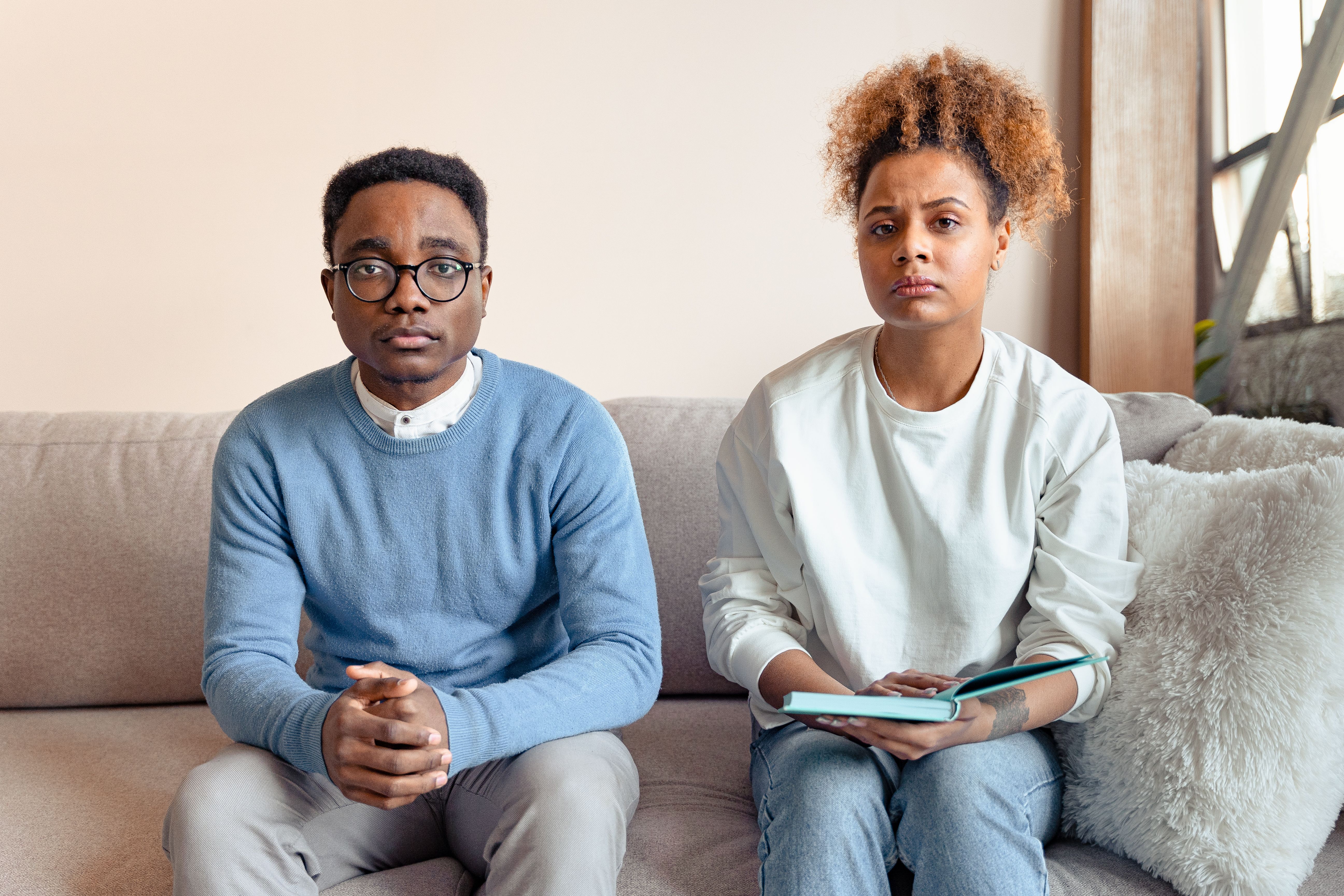 Cena de um casal com expressões preocupadas, sentados em um sofá em um ambiente residencial, simbolizando sentimentos de ansiedade ou preocupação emocional.