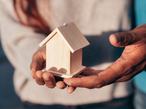 Free Close-up of hands holding a small wooden house, symbolizing real estate or home ownership. Stock Photo
