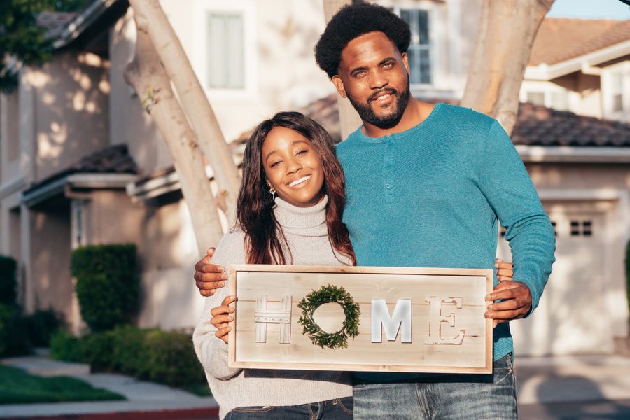 Couple holding a Home sign in front of their new house