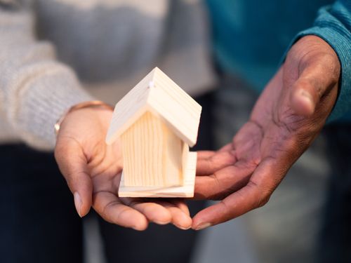Free Hands holding a small wooden house model, symbolizing new home ownership and real estate transactions. Stock Photo