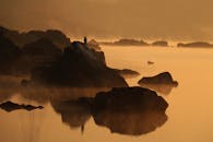 日落时分，薄雾湖上景色宁静，岩石轮廓清晰，一只孤鸟独立