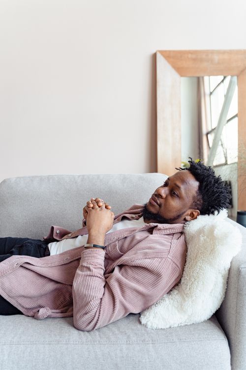 Free Casual black man lying on couch with hands clasped, wearing pink jacket, reflecting relaxation. Stock Photo