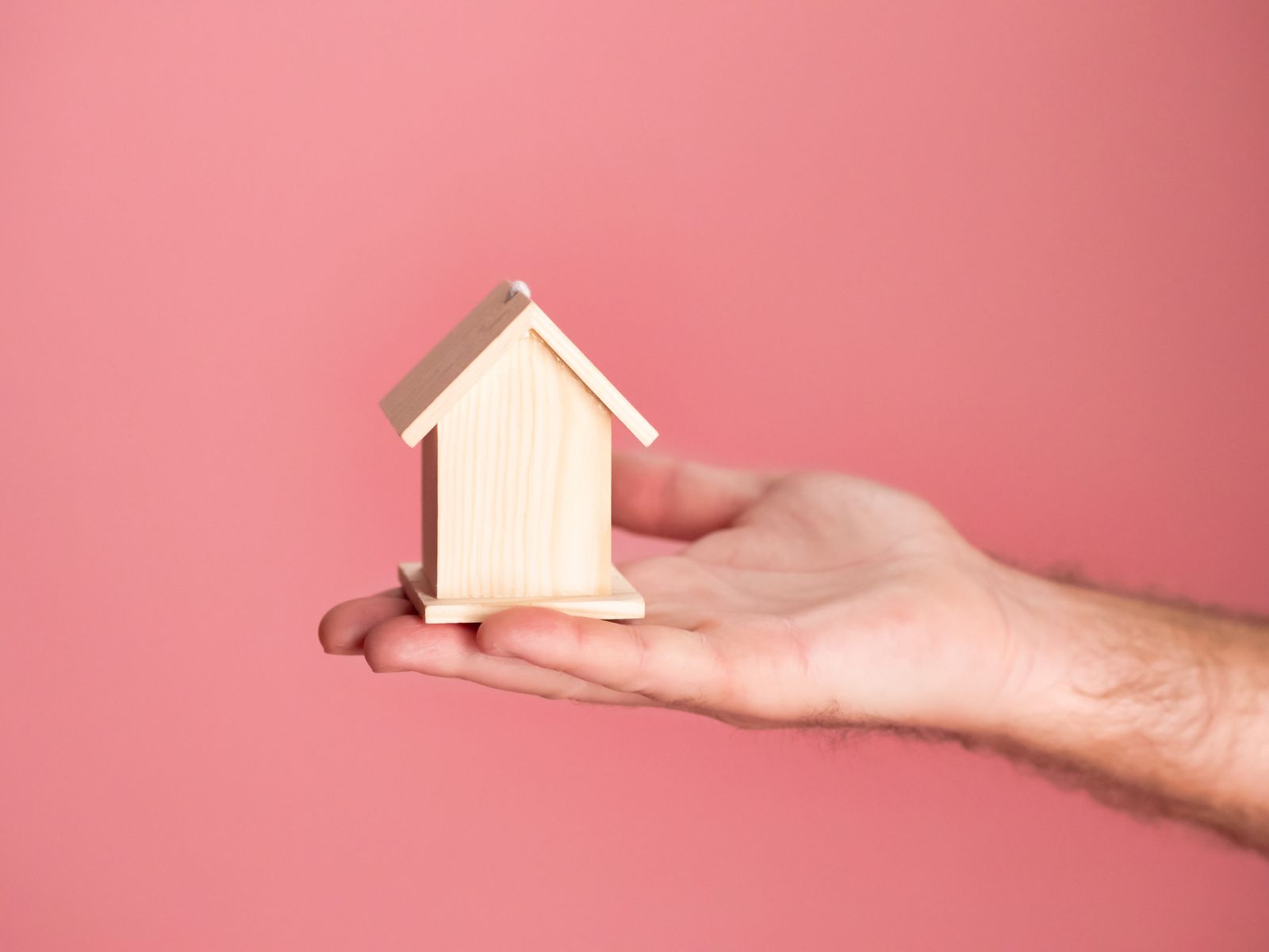 A hand holding a small wooden model house, symbolizing property financing and ownership