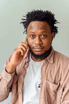 Portrait of a thoughtful man with afro hair having a phone conversation indoors.