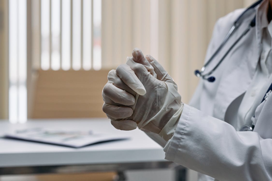 Free Close-up of a medical professional's hands, wearing latex gloves, in a clinical setting. Stock Photo