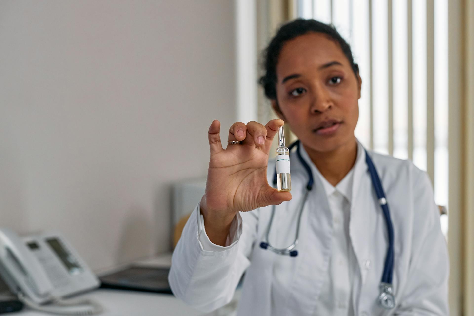 A female doctor in a white coat holding a medical ampoule, illustrating healthcare professionalism.