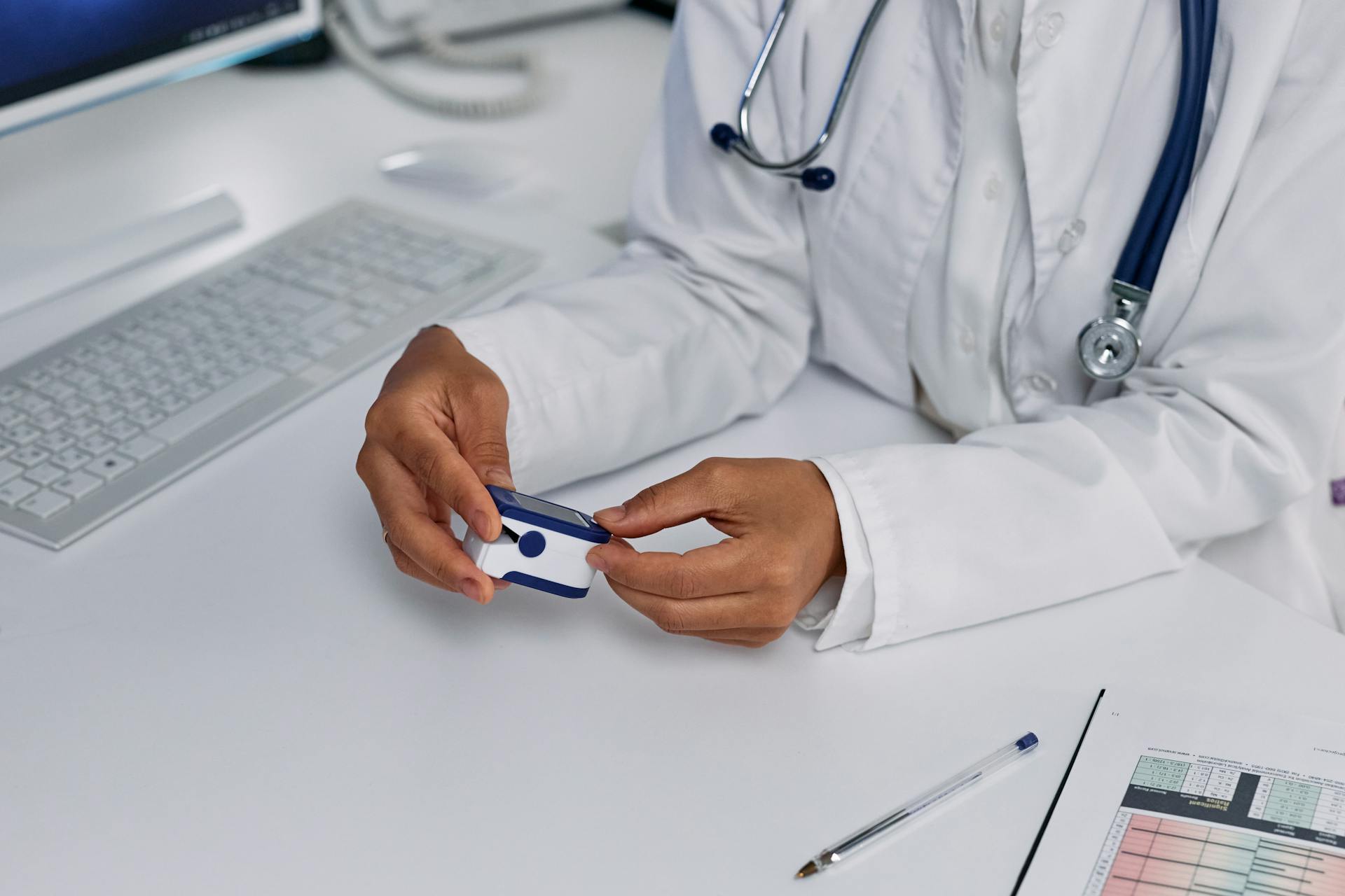 Close-up of doctor using pulse oximeter at medical office desk for vital sign monitoring.