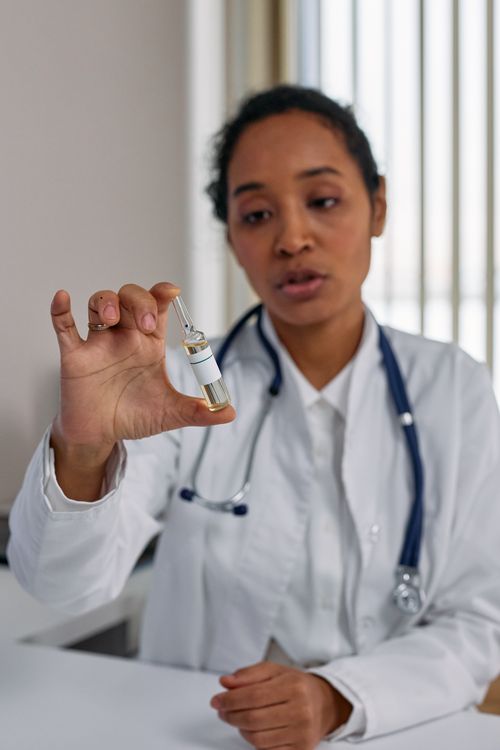 Free Doctor explains vaccine details while holding ampoule in clinic setting. Stock Photo