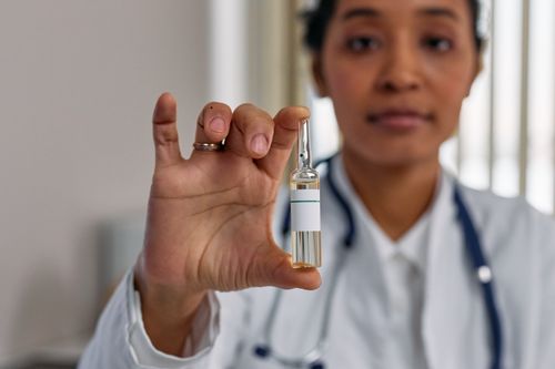Free Healthcare professional displaying a vaccine ampoule in a medical clinic for COVID-19 treatment. Stock Photo