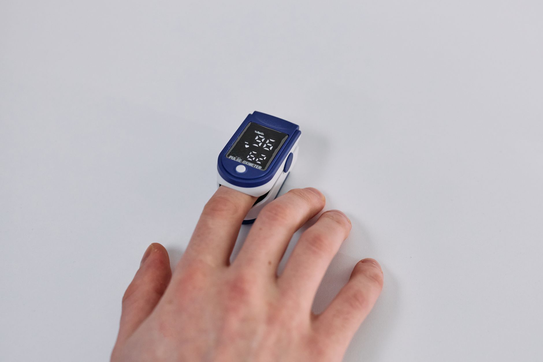 Close-up of a hand using a pulse oximeter to measure oxygen levels on a white background.