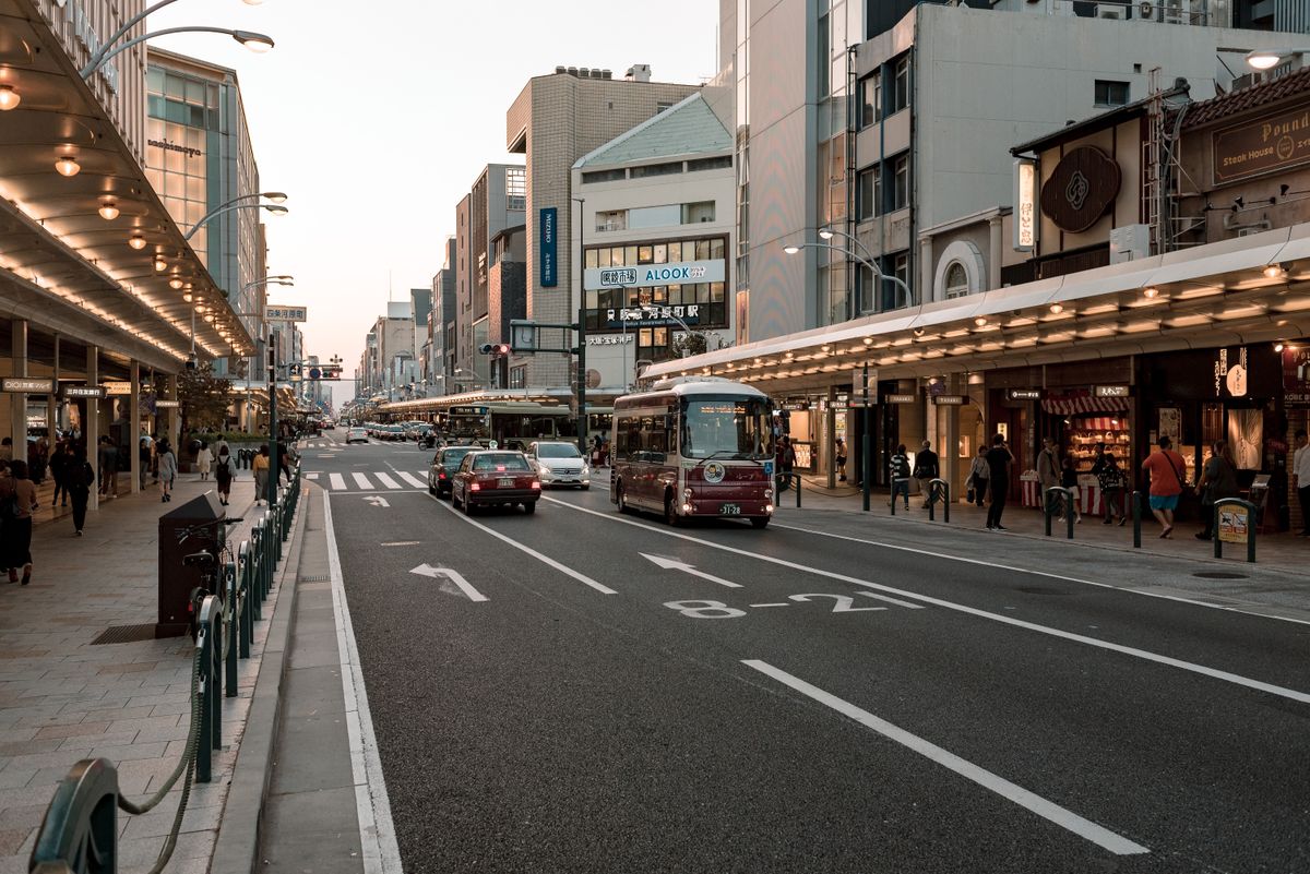 Urban street in Kyoto with cars and pedestrians during sunset, capturing city life.