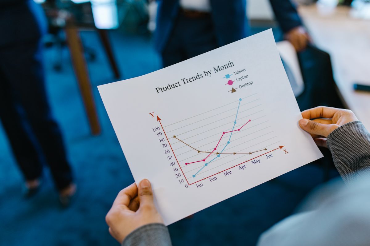 Hands hold a printed line chart of monthly trends for three product lines