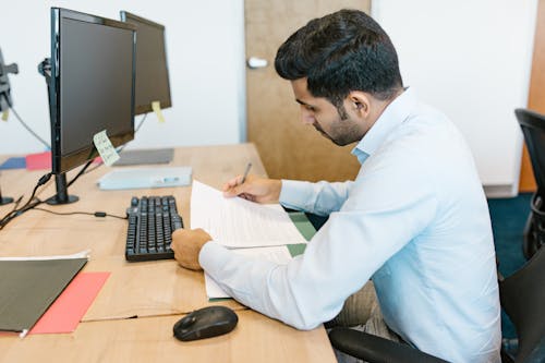 Man in White Long Sleeve Shirt Writing on White Paper