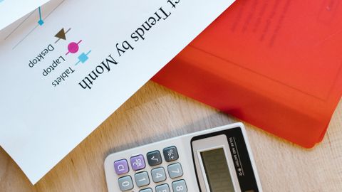 Calculator on desk with business documents and charts detailing product trends.