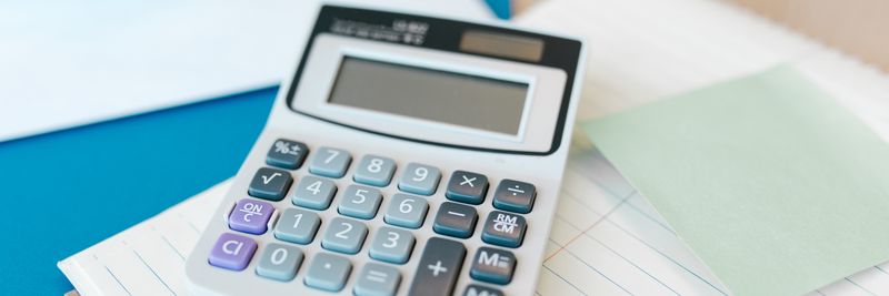 A white calculator on a stack of lined paper with a blue folder, capturing an office setting.