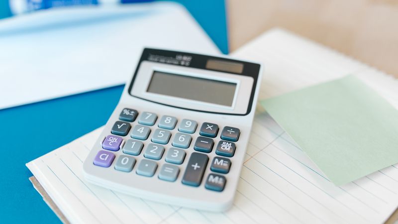 A white calculator on a stack of lined paper with a blue folder, capturing an office setting.