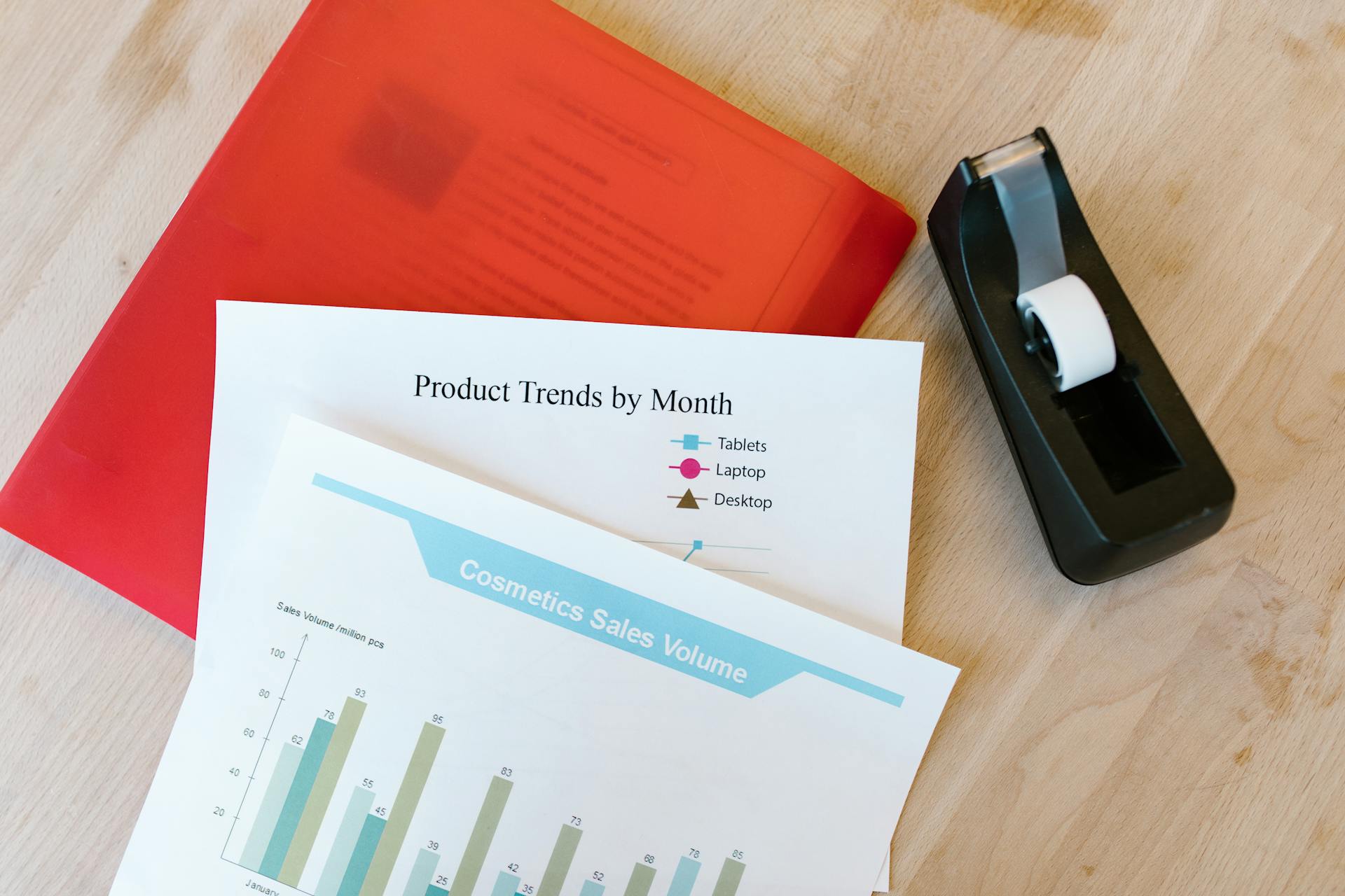 Top view of a desk with sales reports, a red folder, and a tape dispenser, ideal for business and office themes.