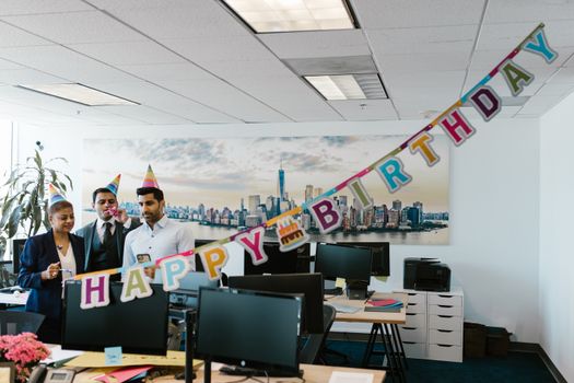 Colleagues celebrate a birthday in the office with party hats and decorations.