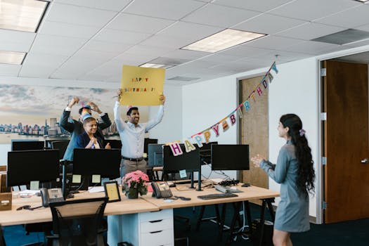A joyful office birthday celebration with colleagues surprising a coworker with a banner and decorations.
