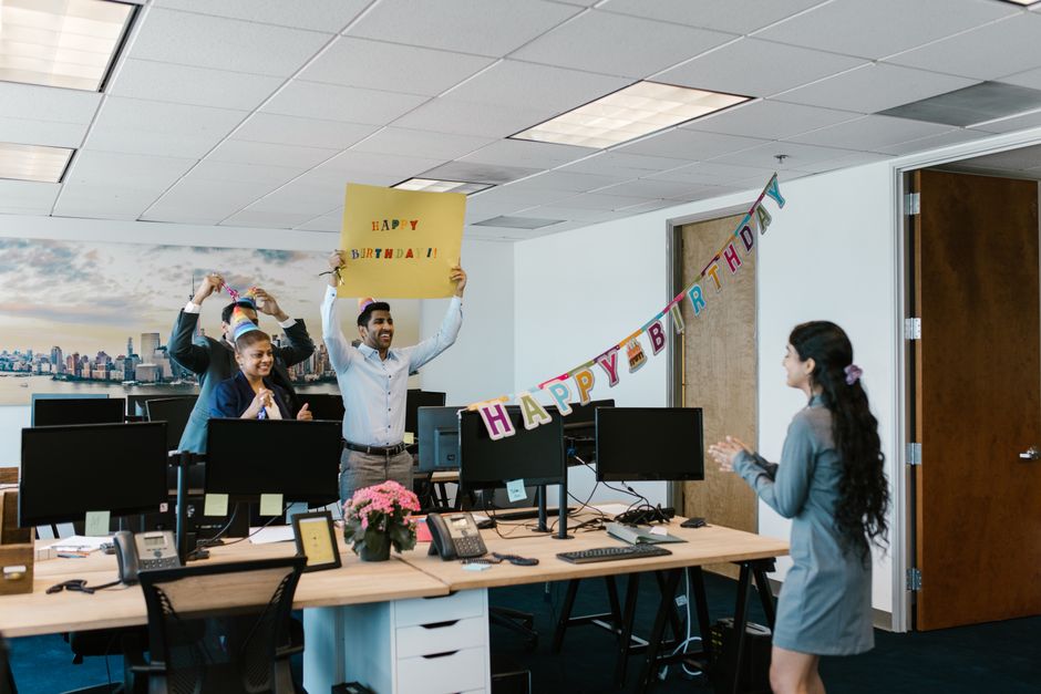 Uma alegre celebração de aniversário no escritório com colegas surpreendendo um coworker com um banner e decorações.