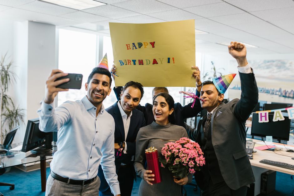 Grupo de colegas celebrando um aniversário no escritório com presentes e um selfie.