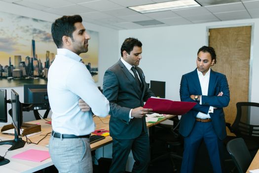 Three businessmen discussing important documents during a meeting in a modern office setting.