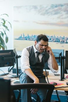 Businessman in office, stressed while on a phone call, expressing frustration.