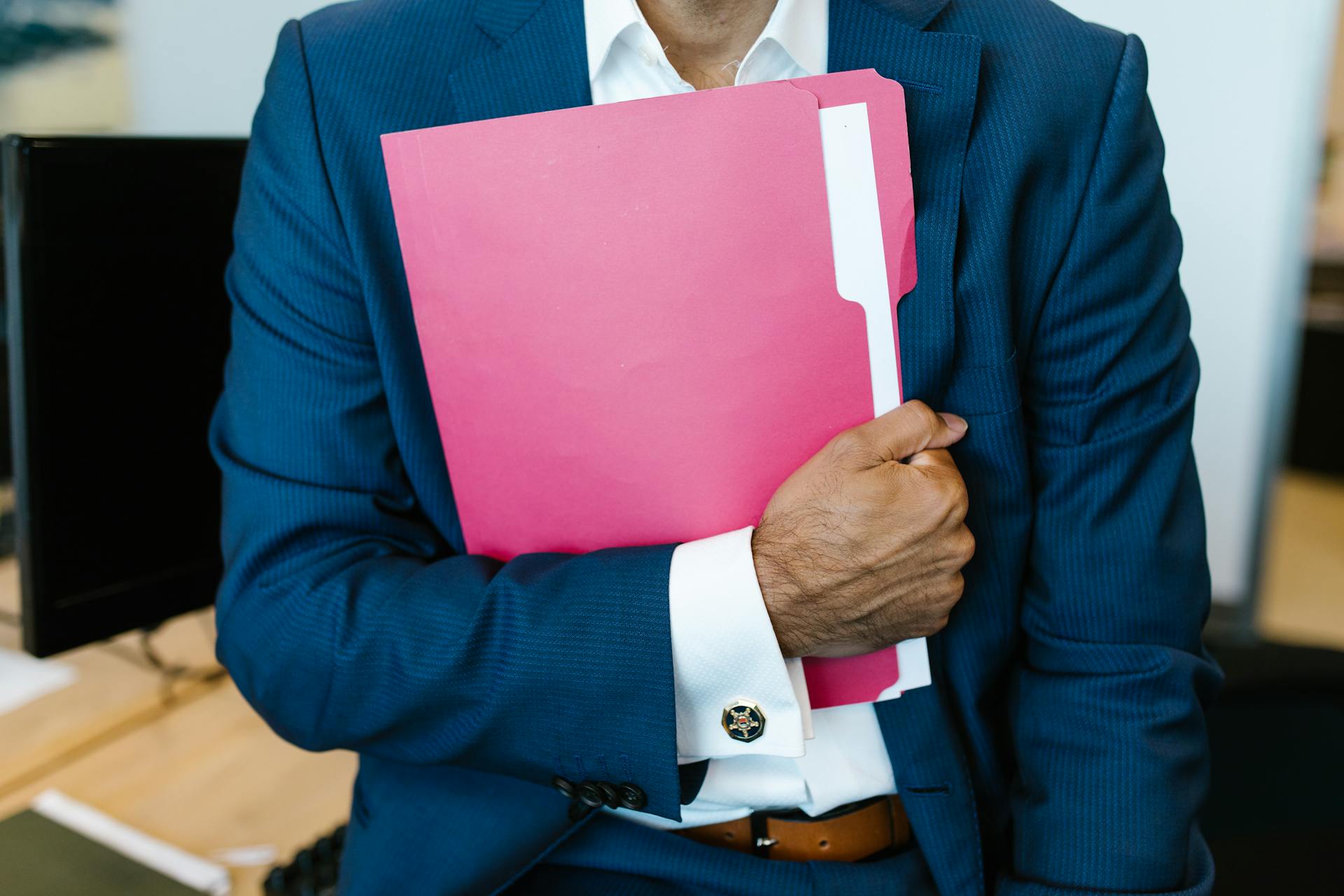 A professionally dressed man holding a pink folder in an office setting.