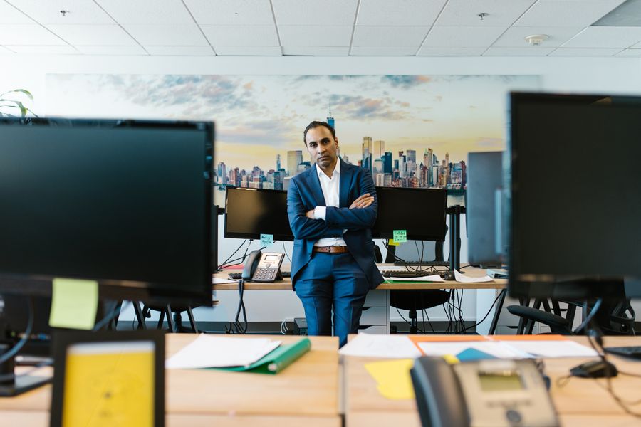 Businessman in a suit stands confidently in a modern office setting with crossed arms.