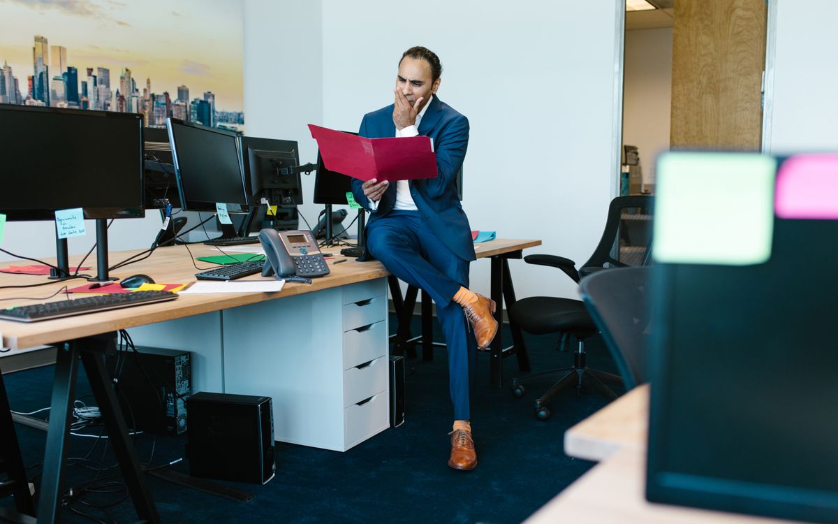 A thoughtful businessman examines documents in a modern office setting.