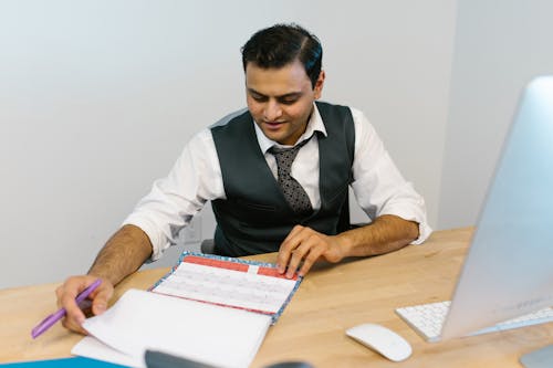 Man in White Dress Shirt and Black Necktie Writing on White Paper