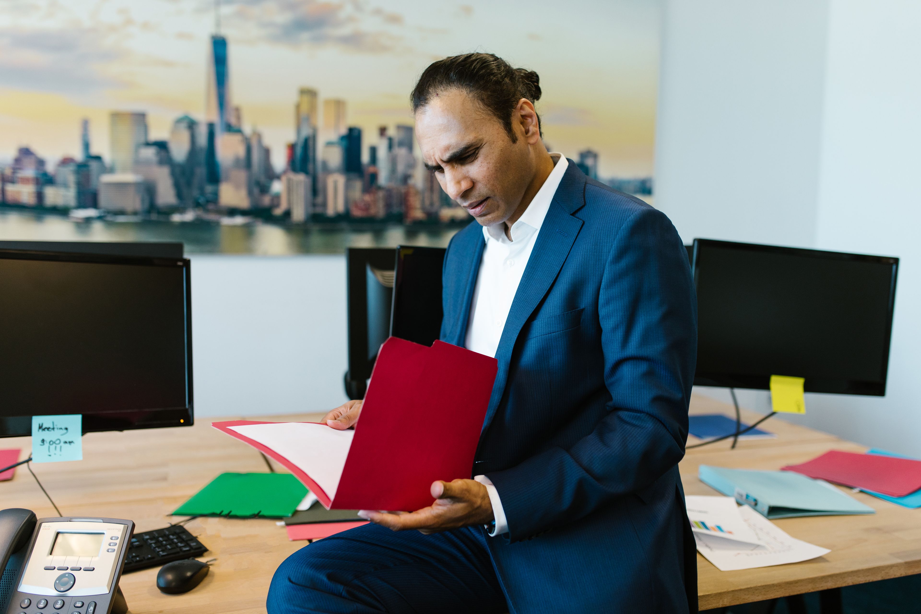 A man in a blue suit holding a folder of documents in an office