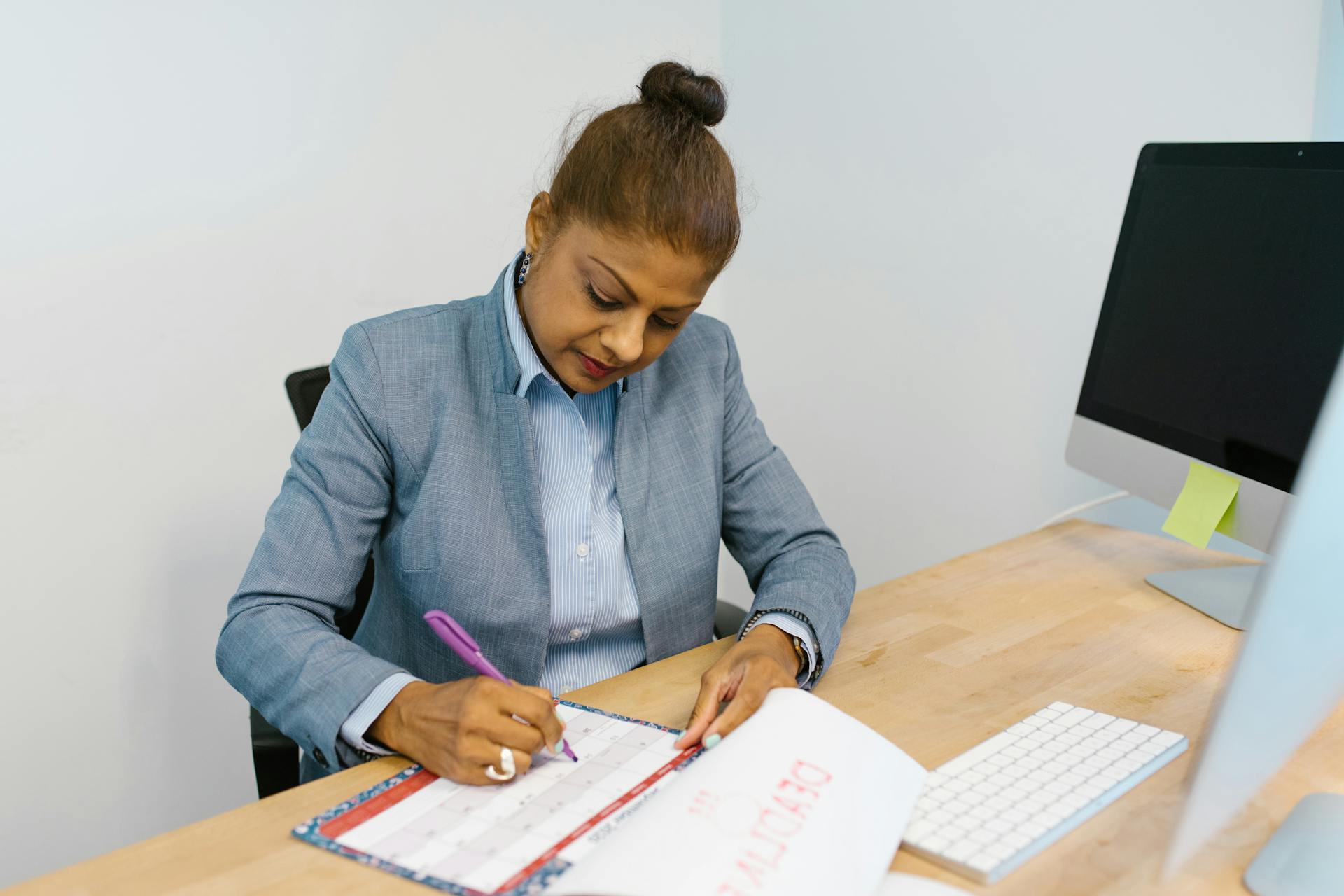 Businesswoman writing plans in a calendar at her office desk.