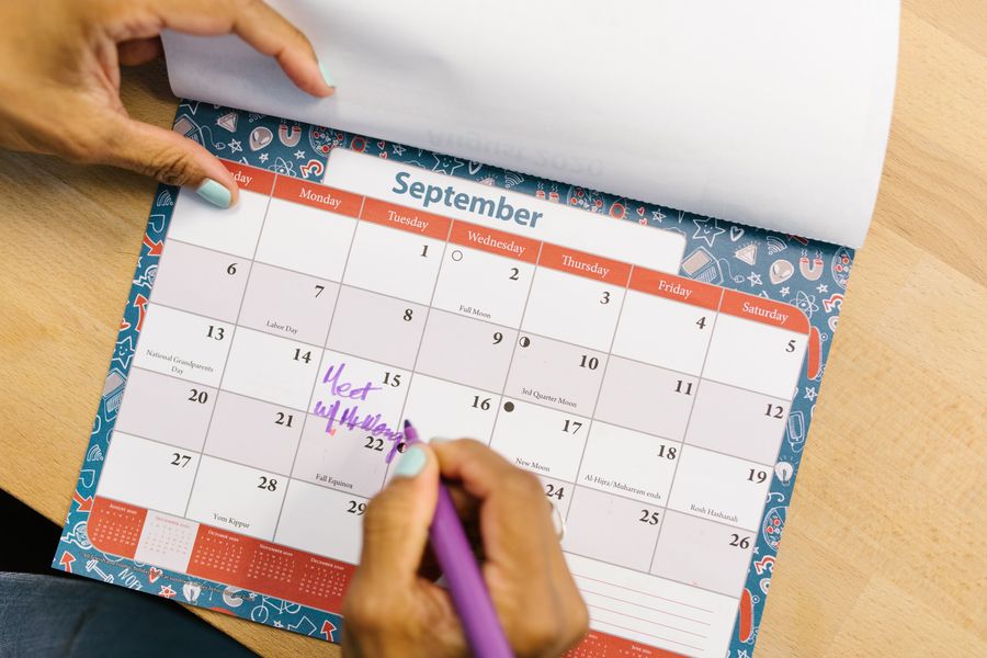 A hand marking a date on a desk calendar with a pen